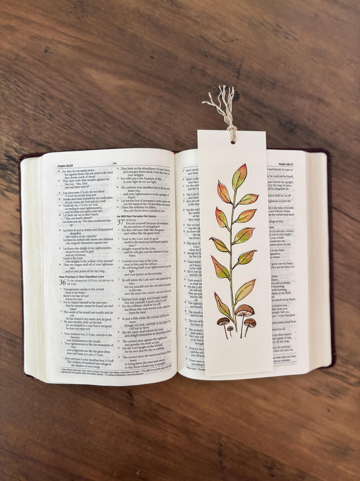 An open Bible book on a wooden table with a decorative bookmark shaped like a leafy plant hanging from the pages.